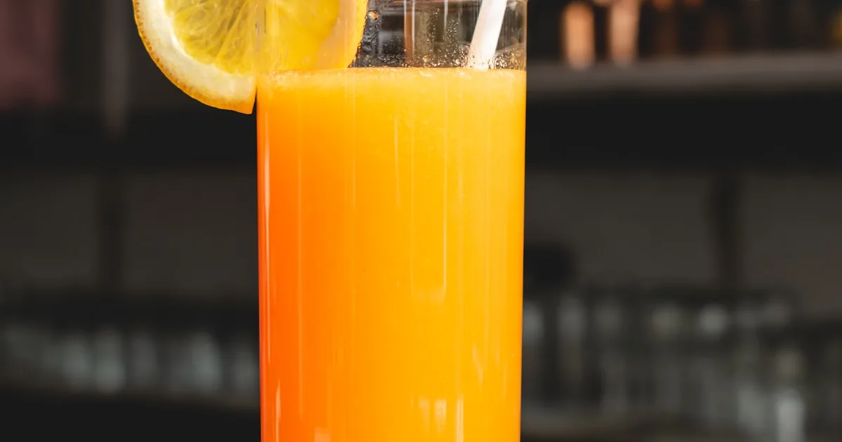 Jus de carotte frais pressé à froid avec carottes entières et oranges en arrière-plan, lumière naturelle ensoleillée