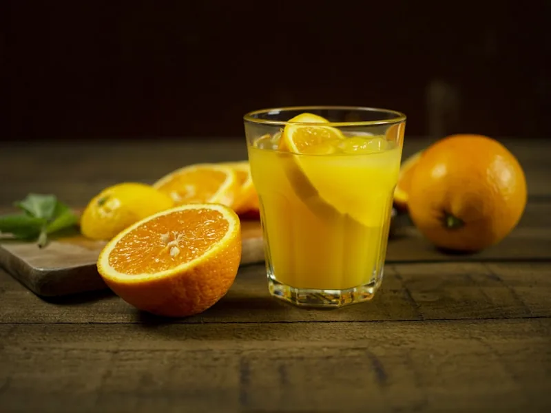 Verre de jus frais pressé à froid orange-carotte avec fruits entiers et gingembre en arrière-plan
